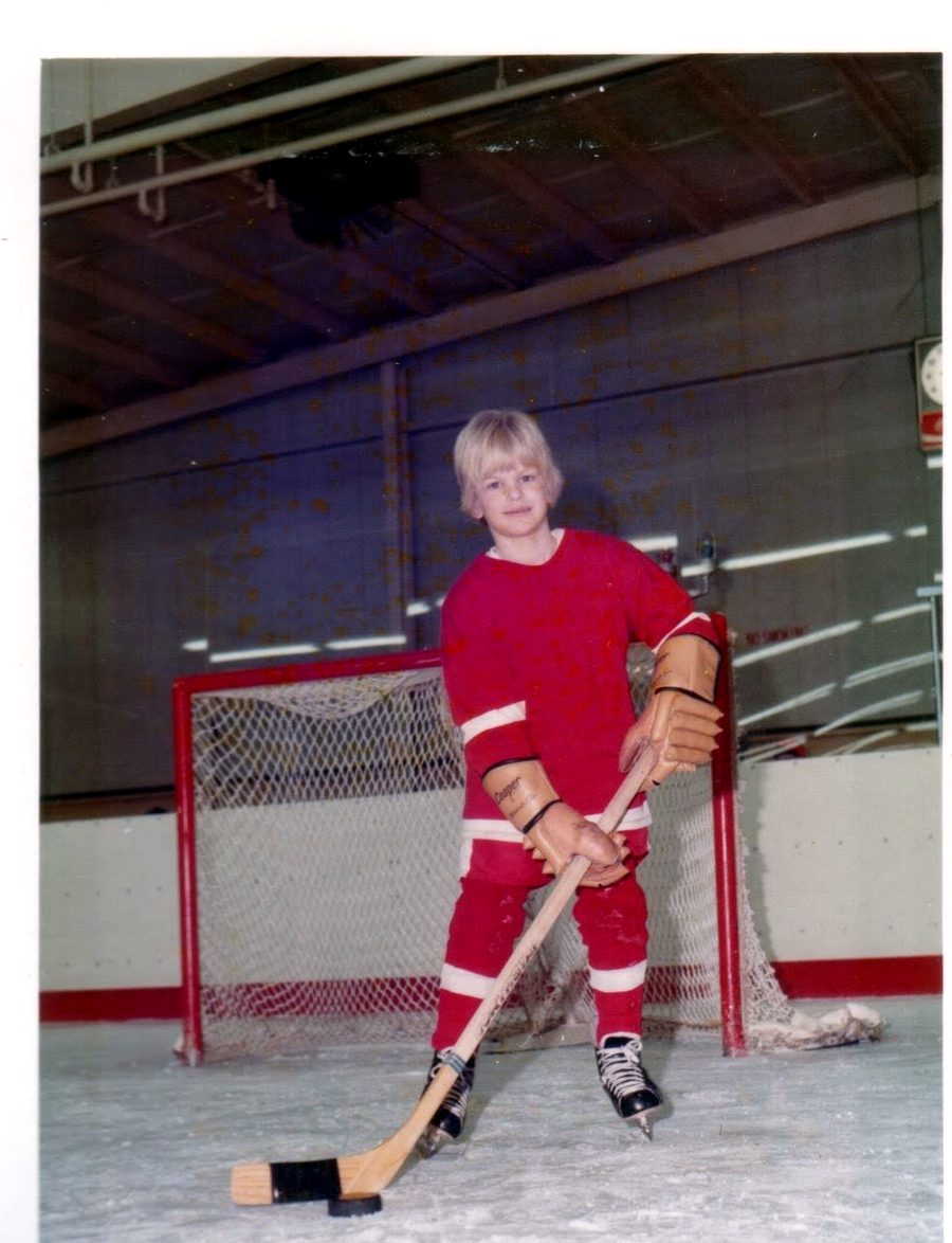 A youth hockey player in a red jersey, stick in hand, standing in front of the goal.
